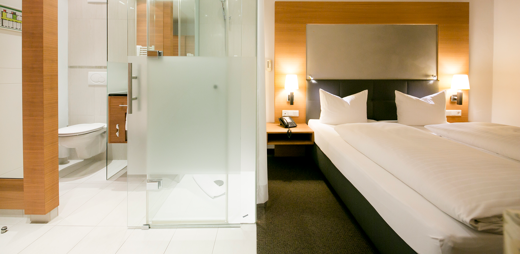 Camera luminosa con bagno moderno e accogliente letto matrimoniale, illuminata in modo soffuso.